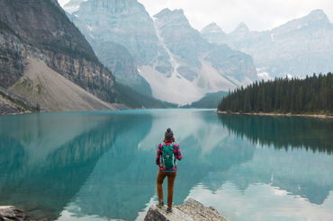 image of Hiker overlooking large lake and mountains during the day.