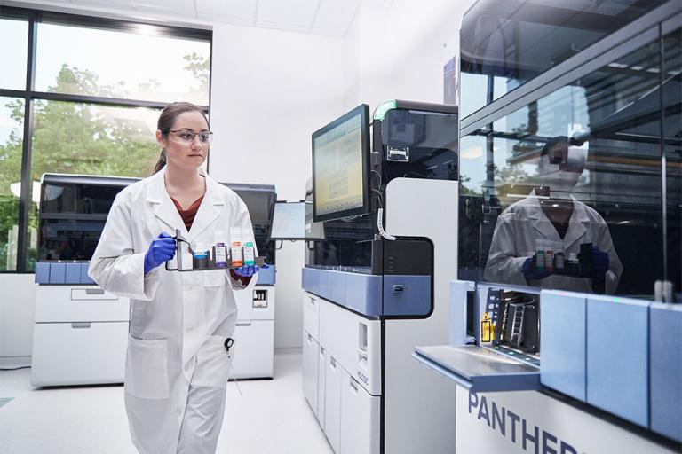 an image of Female lab technician carrying a tray of specimens to insert into Panther system