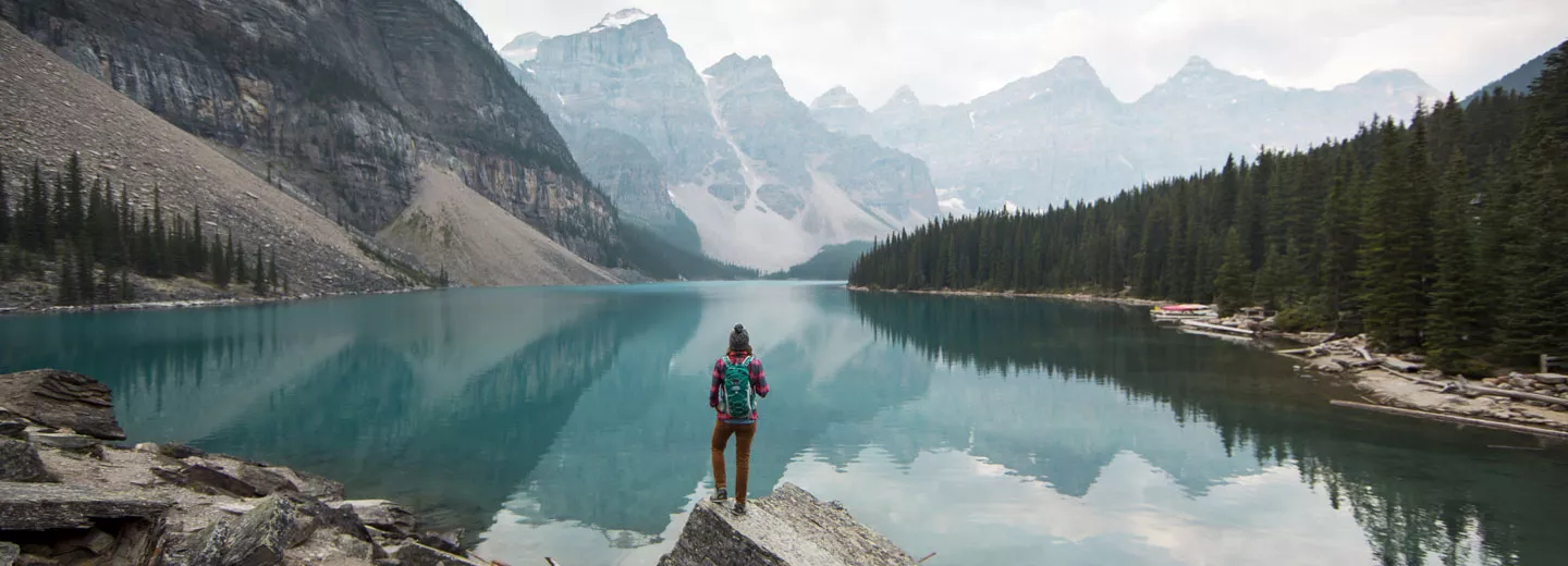 Image of Hiker overlooking large lake and mountains during the day.